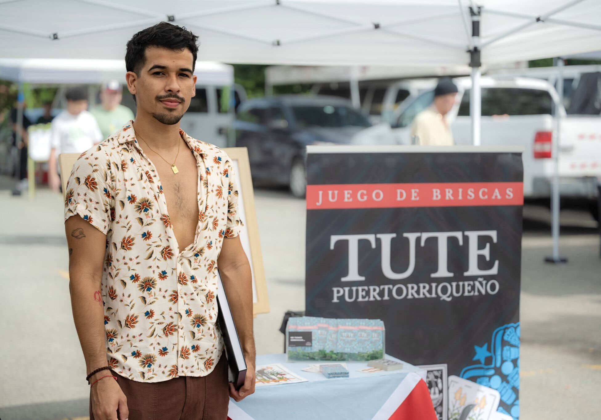 Kevin Mejías standing in front of Tute Puertorriqueño card game banner